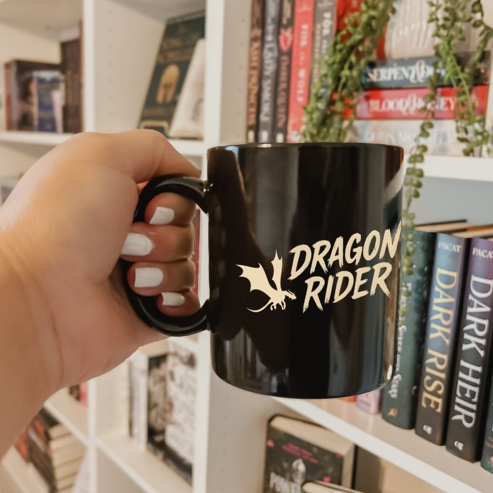 Fantasy reader holding a dragon coffee mug in front of a bookshelf