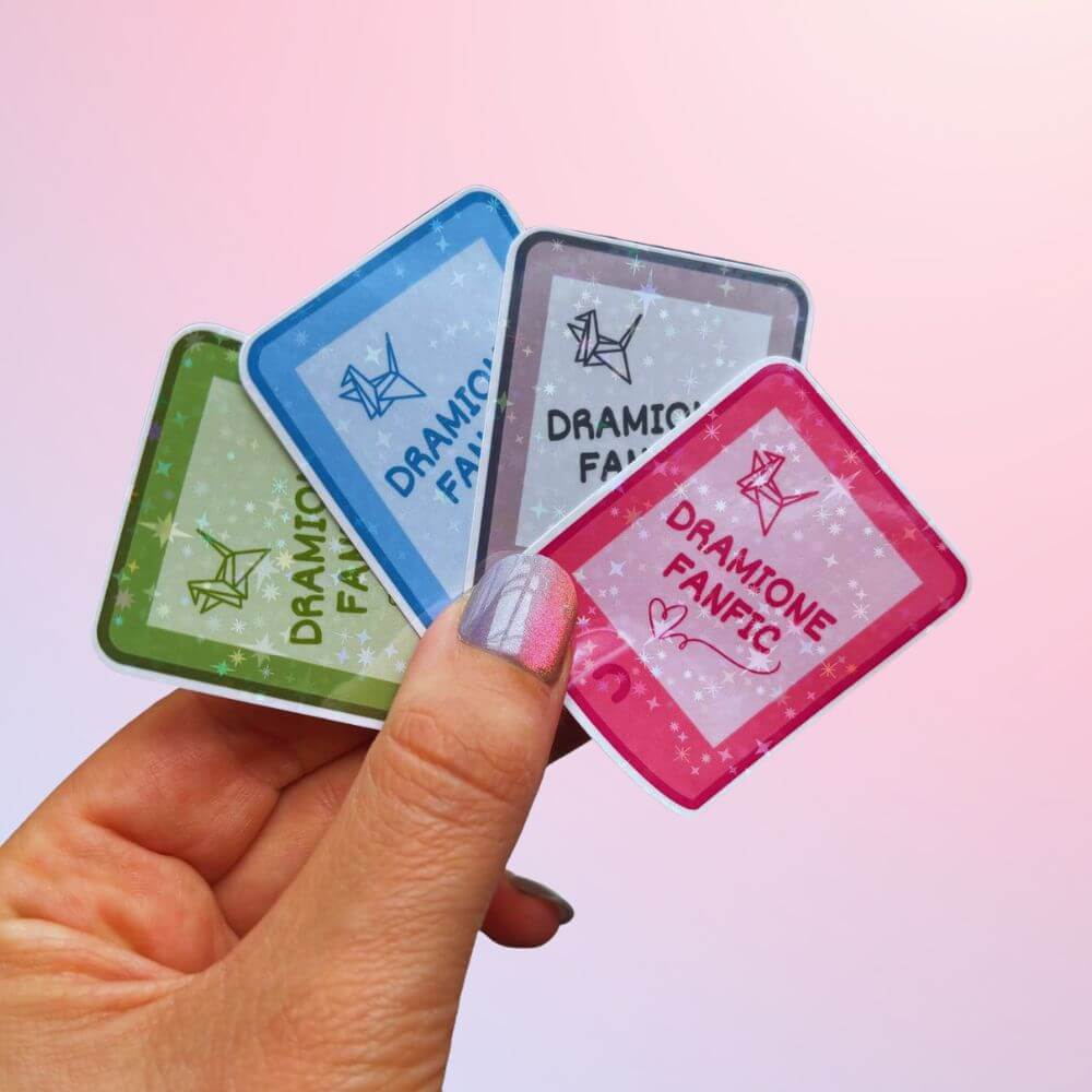 Hand holding holographic Dramione fanfic Kindle stickers in four colors