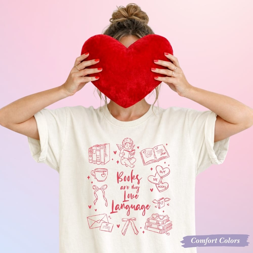 Cream Comfort Colors “Books Are My Love Language” t-shirt with Valentine icons; model holding red heart pillow; Valentine’s Day gift for book lover.