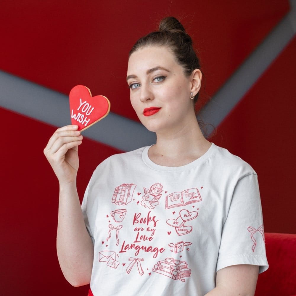 Model holding heart pillow wearing “Books Are My Love Language” tee with Valentine doodles and sleeve bow, gift for reader.